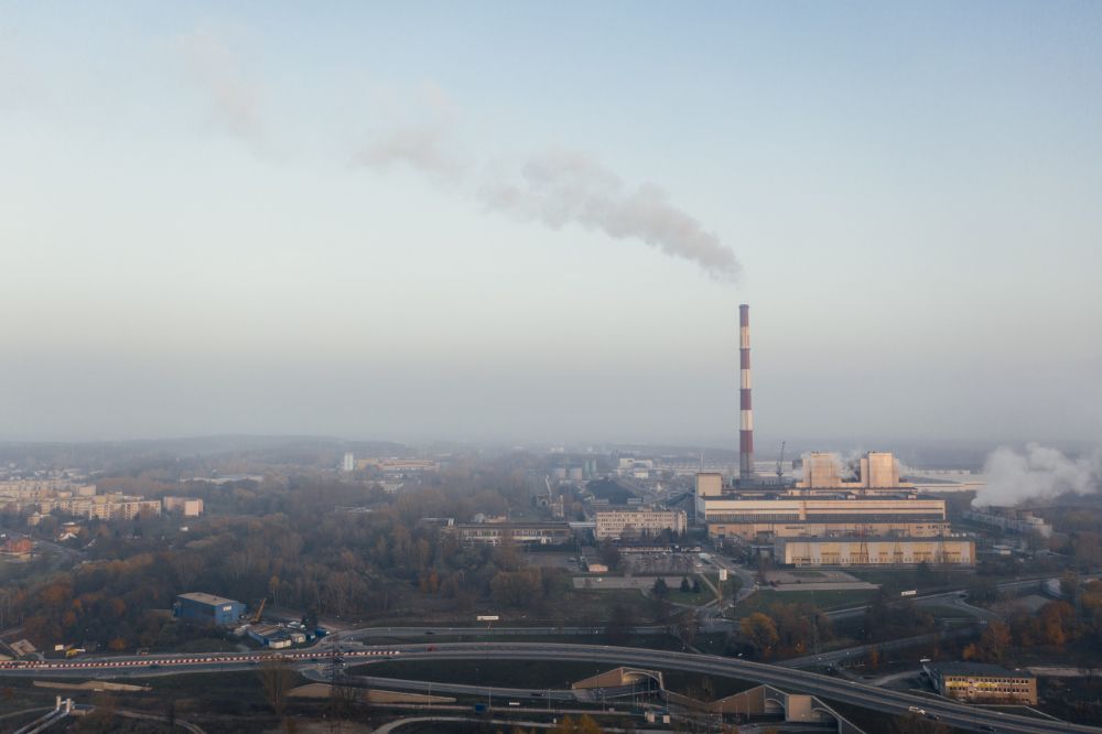 Factory with red and white stripy chimney emitting smoke next to motorway.