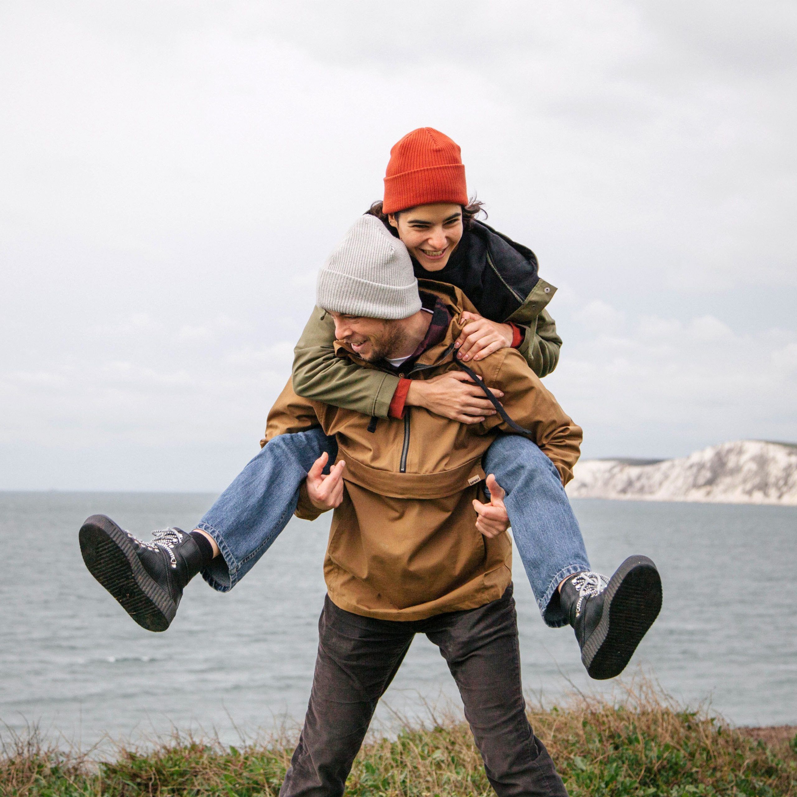 A couple enjoy a piggyback ride by the coast while wearing matching Rapanui beanies